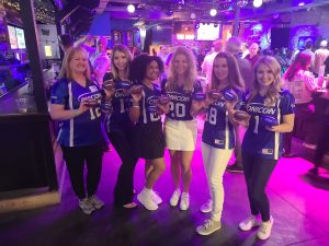 A group of smiling women holding ONICON & Air Monitor branded footballs at the AHR Expo hospitality event, celebrating with a fun and energetic atmosphere