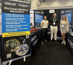 ONICON and Air Monitor trade show booth showcasing flow and energy measurement solutions for data centers, with banners highlighting benefits like real-time accuracy, sustainability, and risk reduction. Three representatives stand in front of the display featuring instruments and branded materials.